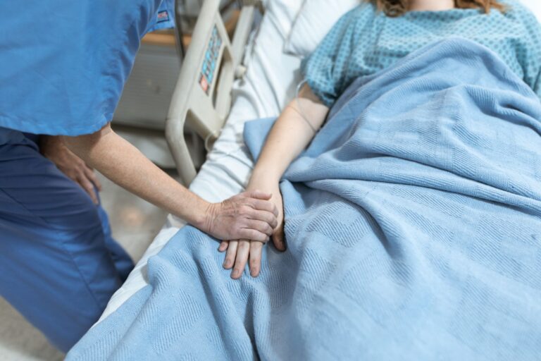 Danke an Pflegepersonal – Pflegekraft hält tröstend die Hand einer Patientin