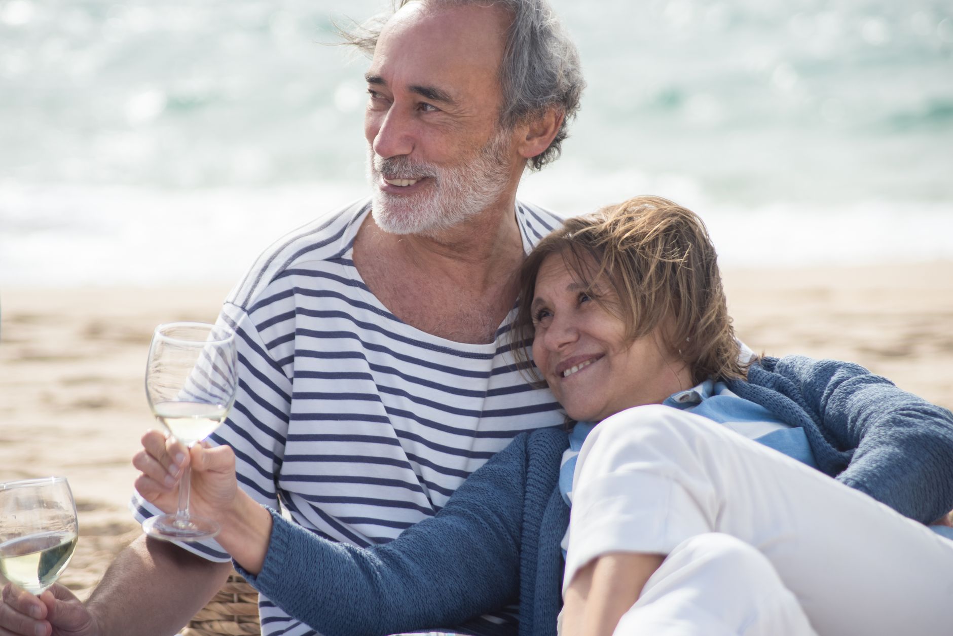 Glückwünsche zum Rentenbeginn – älteres Paar genießt Wein am Strand