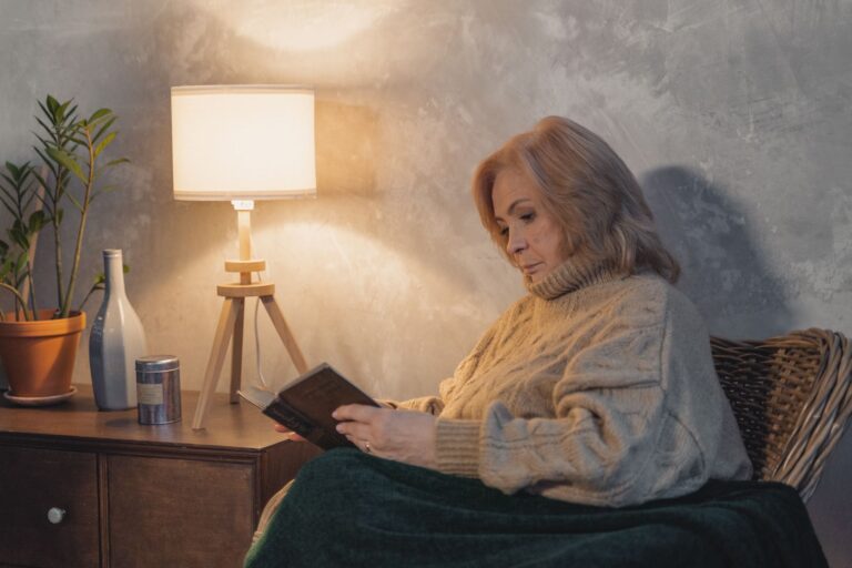 Gute Beleuchtung in der Wohnung – Seniorin liest bei warmem Lampenlicht