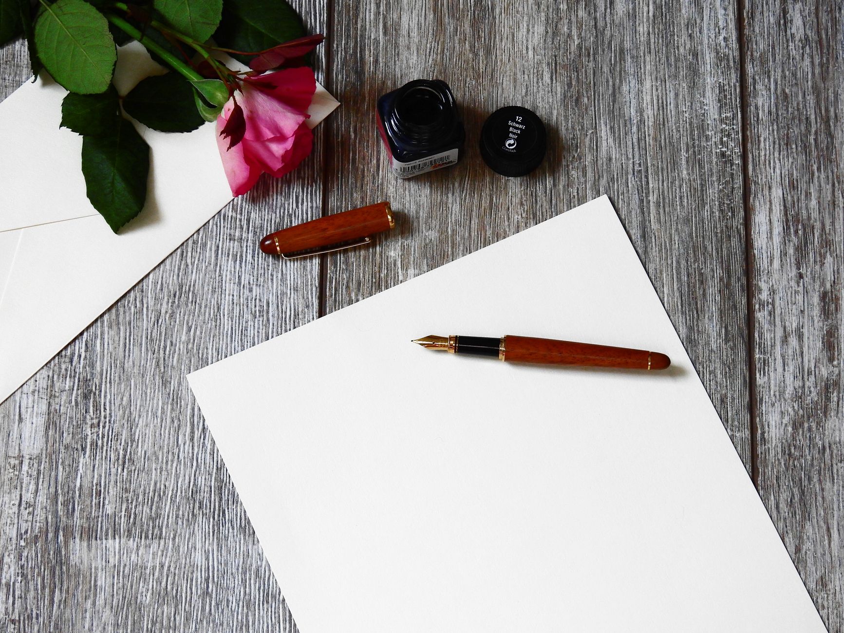 Trauerkarte Umschlag beschriften – Füller, Rose und Papier auf einem Holztisch